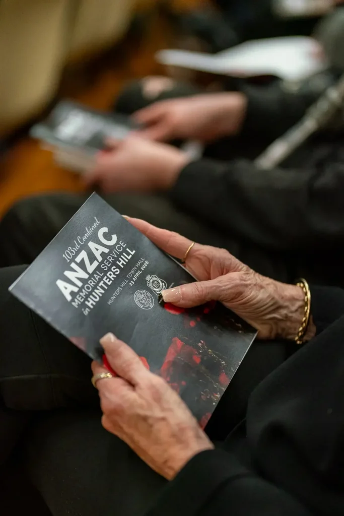 Elderly attendee holding official Combined ANZAC Memorial Service program booklet