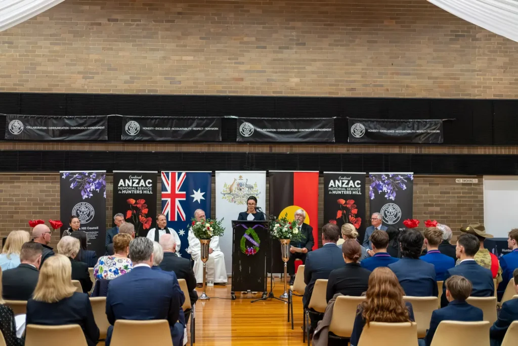 Wide shot of audience attending ANZAC memorial service inside decorated community hall