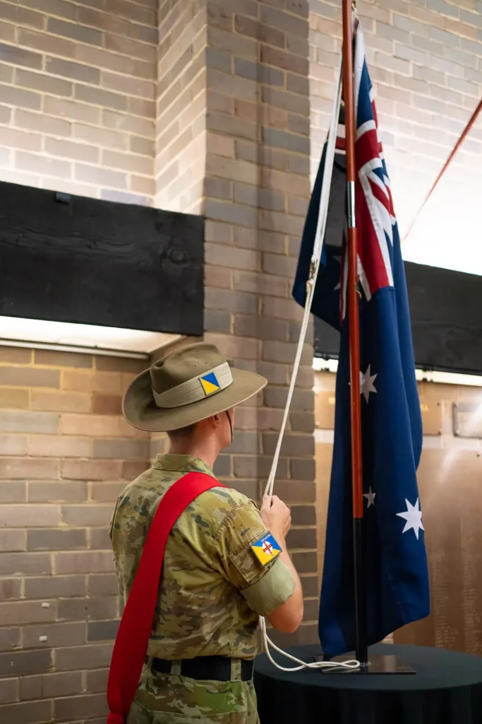 Australian soldier raising the national flag inside memorial hall during ceremony