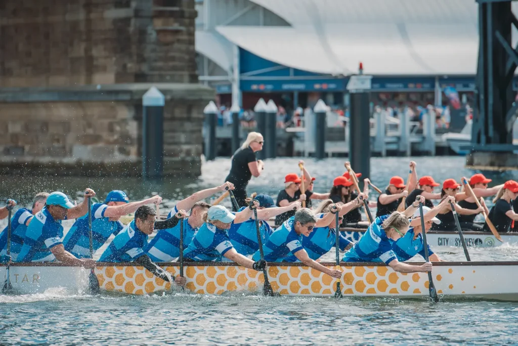 Close-up of a blue-uniformed dragon boat crew paddling hard during a Sydney harbour race