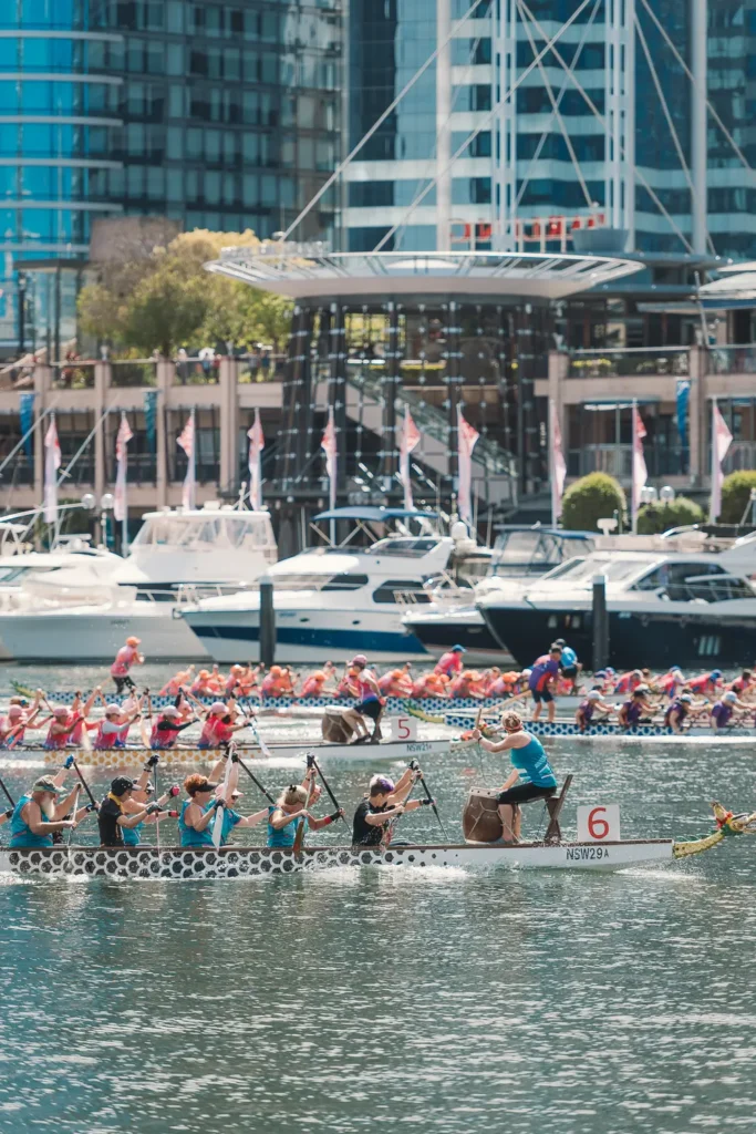 Community dragon boat crew paddling through Darling Harbour with Sydney waterfront buildings behind them