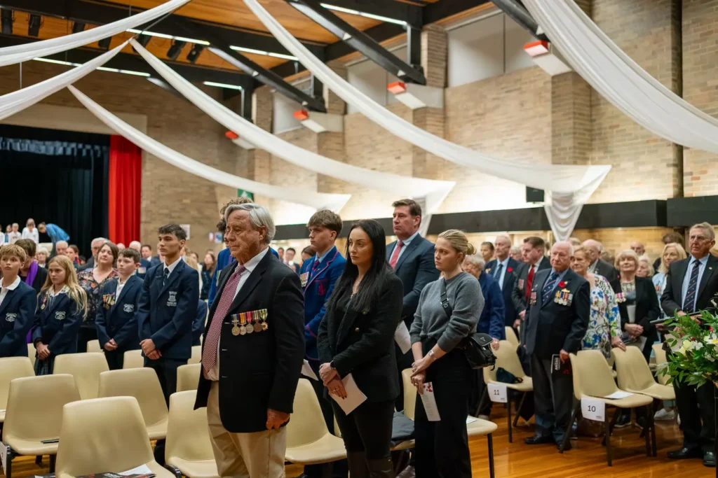Community members, veterans, and students standing respectfully during ANZAC memorial service