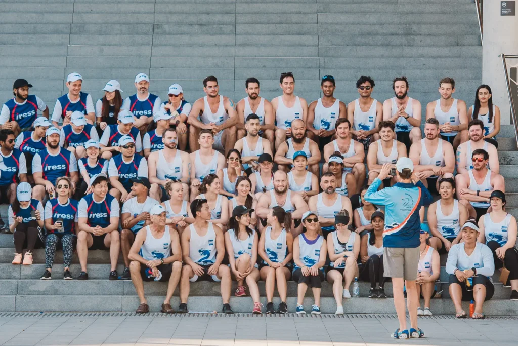 Large corporate dragon boat teams posing for a group photo on harbour steps