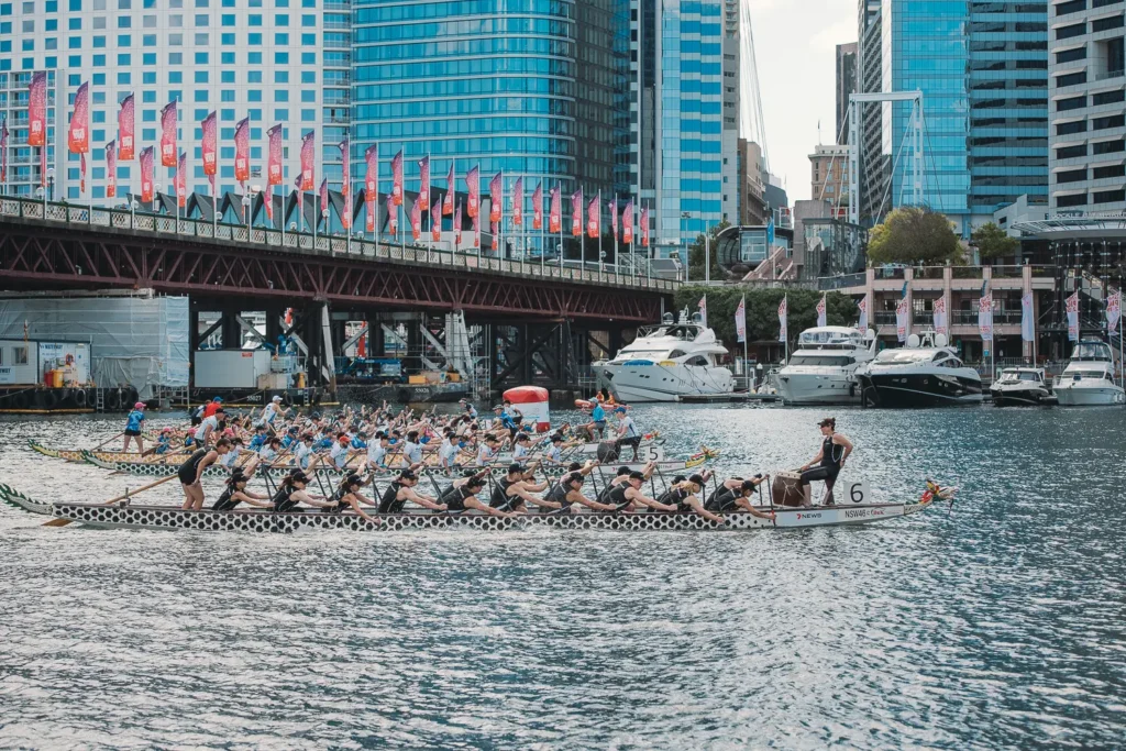 Multiple dragon boat teams launching into a race at Darling Harbour with Sydney city skyline and Pyrmont Bridge in the background