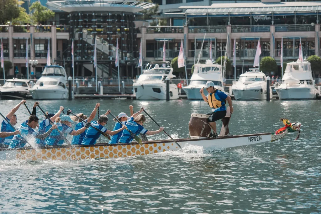Female drummer guiding a dragon boat crew paddling across Darling Harbour during competition