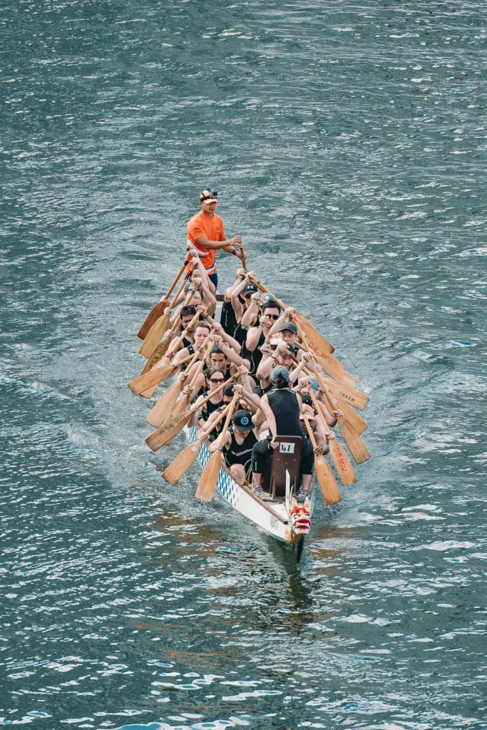 Front-facing view of dragon boat crew paddling in tight formation on harbour water