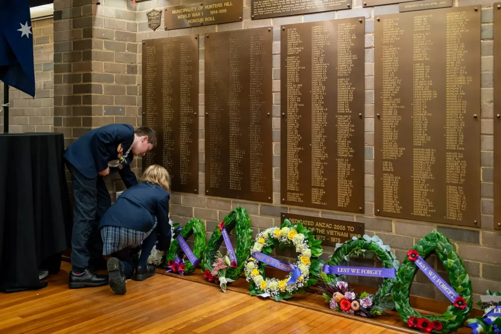 School students placing commemorative wreaths beneath World War honour roll plaques