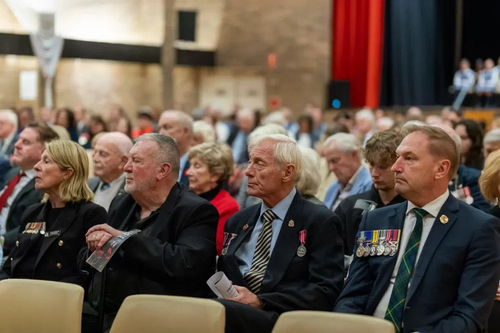 Veterans and attendees seated during ANZAC memorial ceremony wearing medals and formal attire
