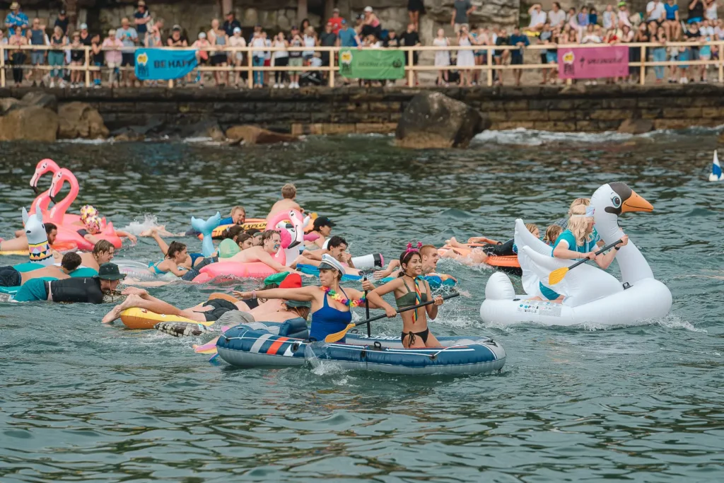 Participants paddling and swimming with colourful inflatables during the Manly Inflatable Boat Race