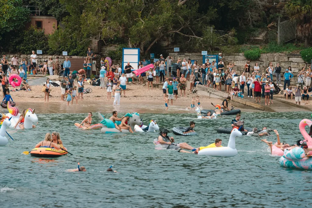 Spectators watching participants on unicorn inflatables near the Manly shoreline