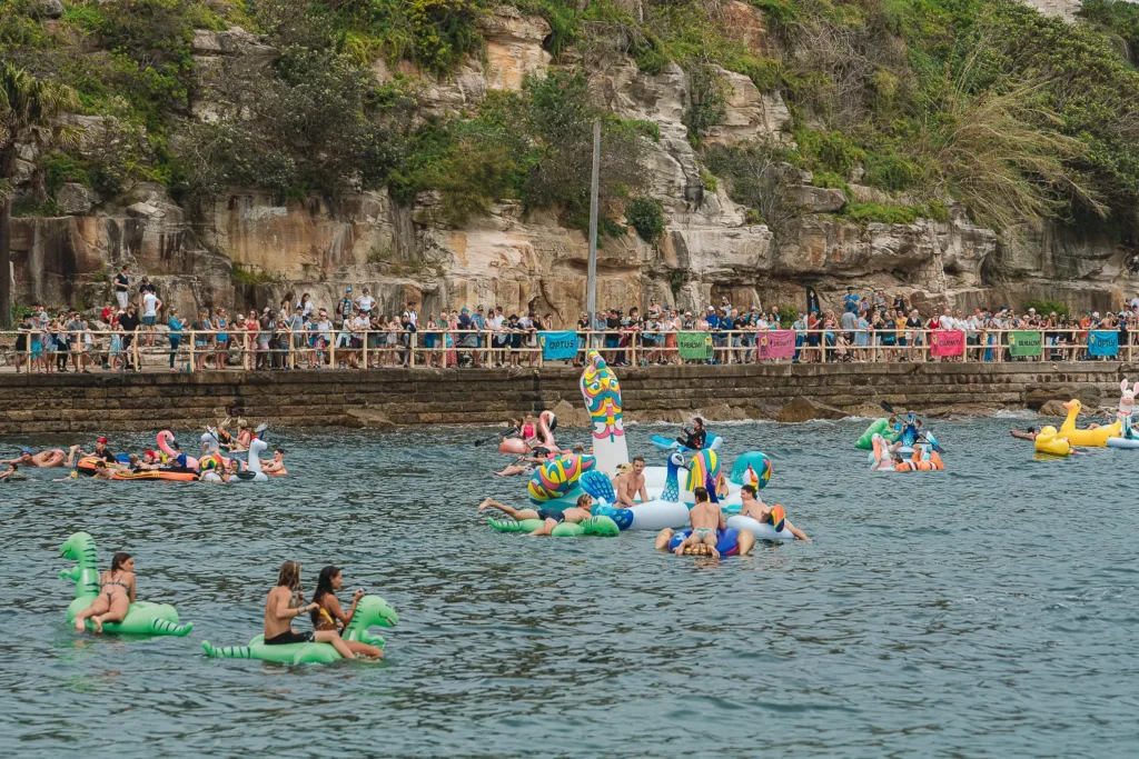 Giant colourful peacock inflatable surrounded by racers and spectators at Manly