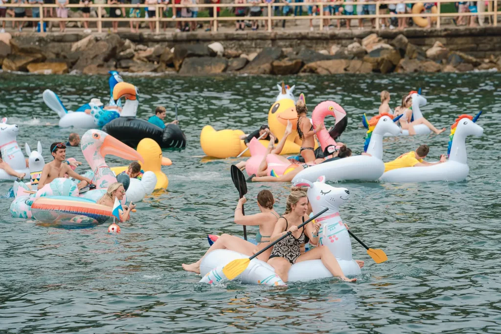 Women paddling a white llama inflatable among colourful novelty floats at Manly