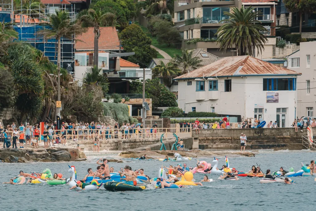 Colourful inflatable racers passing the crowded Manly shoreline