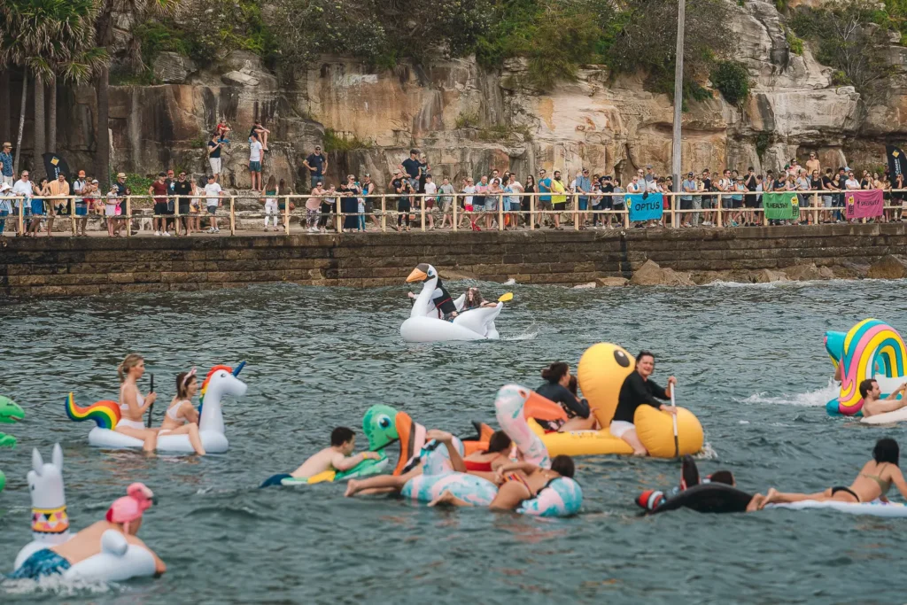 Colourful inflatable boats crossing the water in front of spectators along Manly waterfront