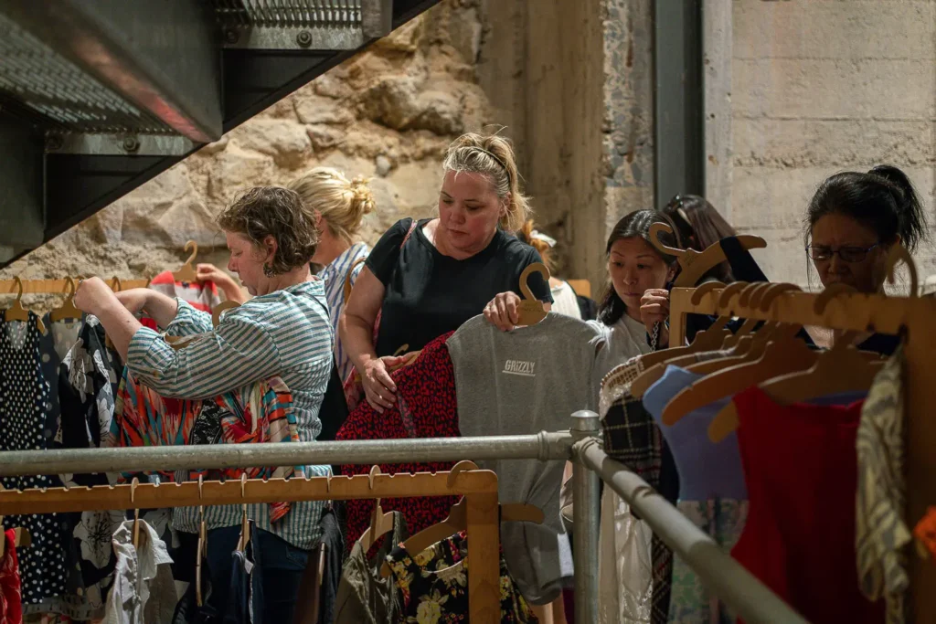 Shoppers browsing secondhand clothing racks at a sustainable fashion market