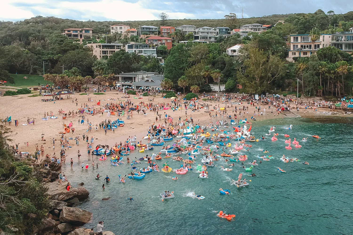 Aerial view of crowds and colourful inflatables entering the water at Shelly Beach in Manly
