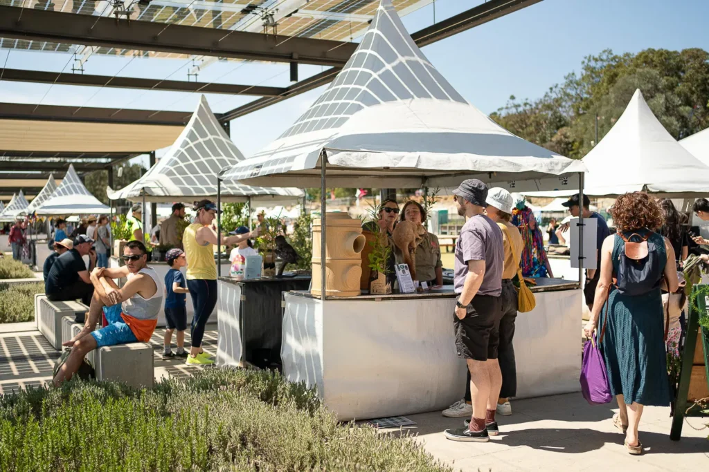 Visitors exploring sustainability stalls under white tents at an outdoor festival