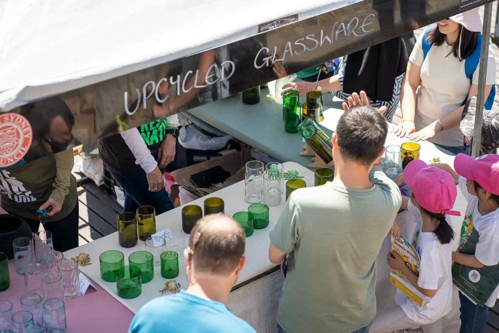 Visitors browsing colourful upcycled glassware at a sustainability market stall