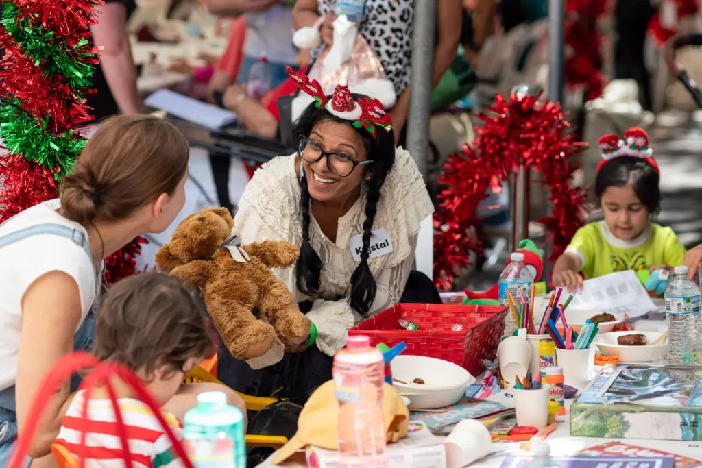 Volunteer with a teddy bear chatting with families at the Wayside Chapel Christmas activities