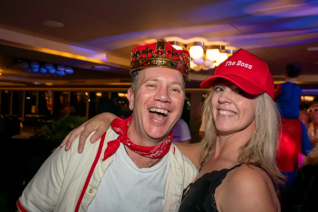 Smiling guests wearing a crown and The Boss cap at a corporate costume party