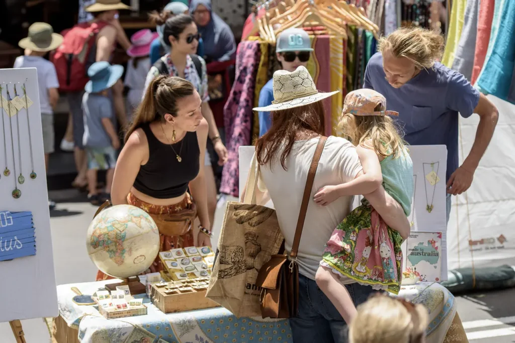 Mother holding her child while browsing handmade jewellery at a colourful Glebe Street Fair market stall