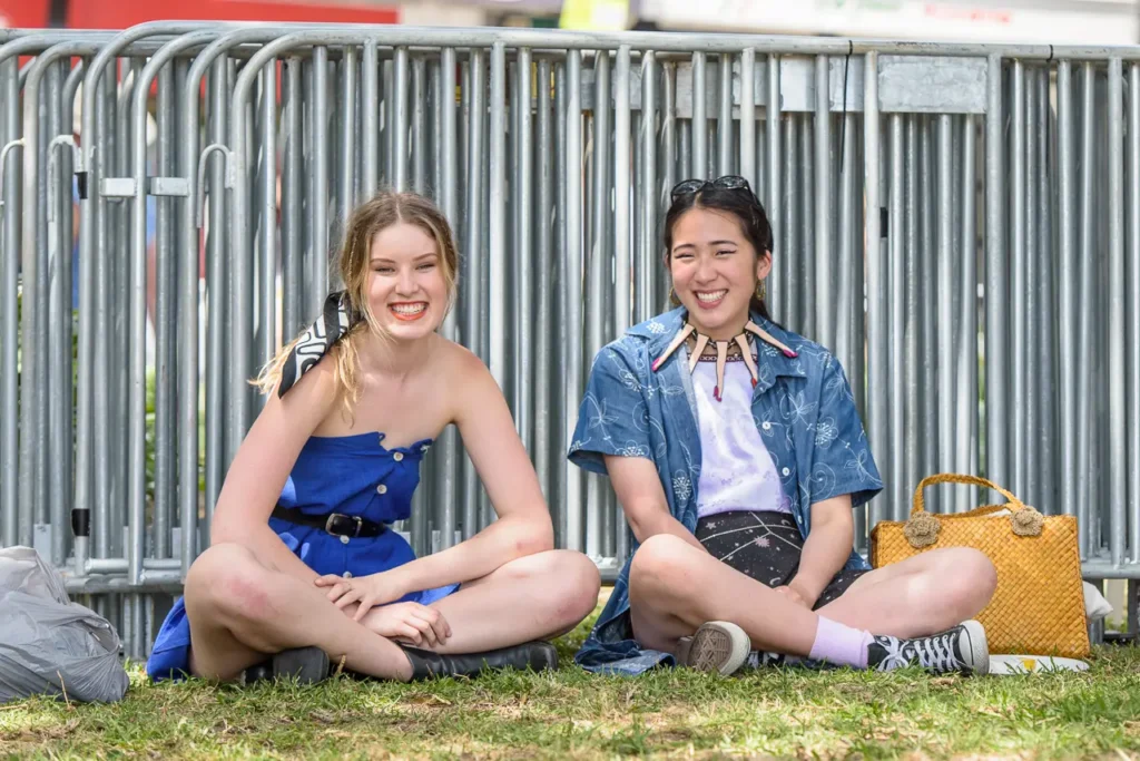 Two smiling friends sitting on the grass and enjoying the relaxed atmosphere of Glebe Street Fair Sydney