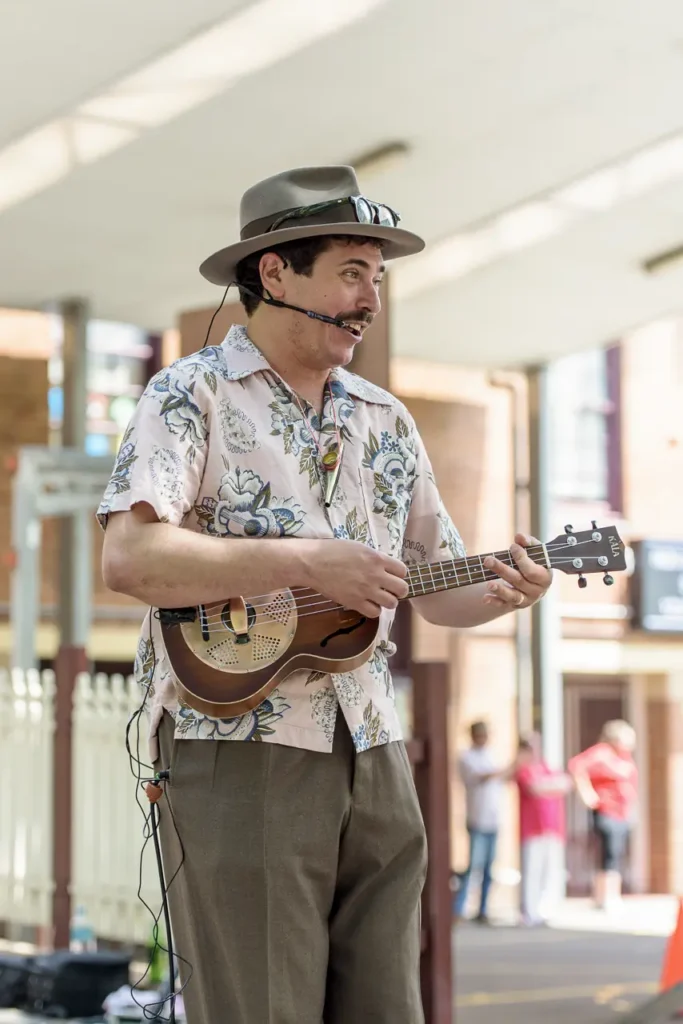 Street musician wearing a hat playing ukulele and performing at Glebe Street Fair Sydney