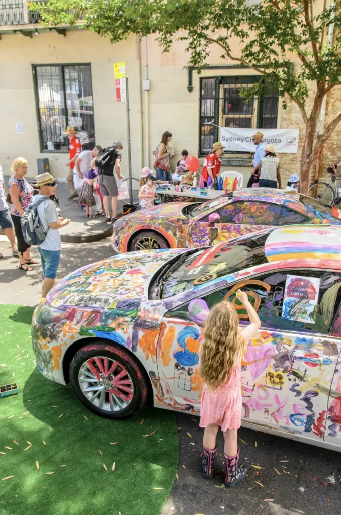 Child painting a colourful Toyota car during an interactive brand activation at Glebe Street Fair Sydney