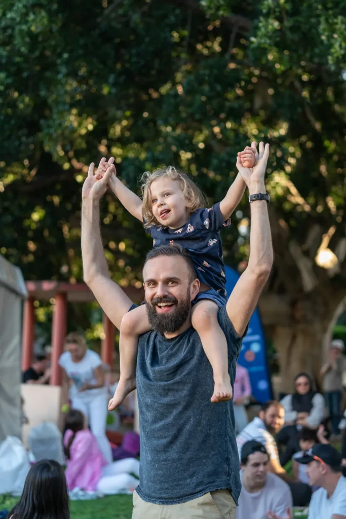 Happy father carrying his young child on his shoulders at Sunset Series 2022 in North Sydney